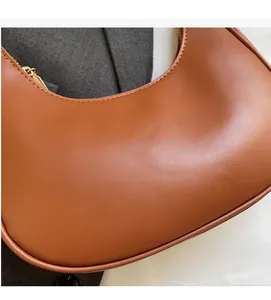 Close-up of brown leather crescent bag with matte finish and gold zipper details