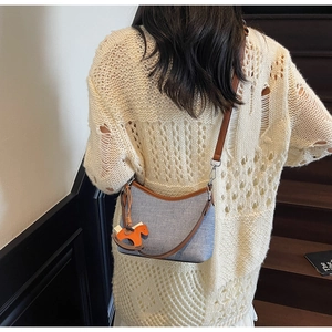 Close-up of blue canvas bucket bag with brown leather trim and orange horse charm