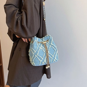 Détail du sac seau en jean effiloché avec chaîne dorée et pendentifs en perles
