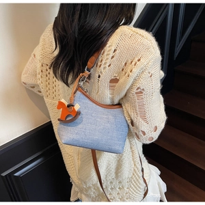 Close-up of texture blue fabric shoulder bag with brown leather trim and horse charm