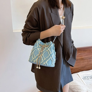 Gros plan du sac seau en denim bleu clair avec texture matelassée et chaîne perlée