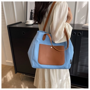 Detail of blue canvas tote bag with brown leather pocket and long shoulder strap