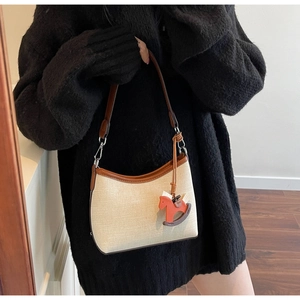 Detail of minimalist beige canvas shoulder bag with brown leather trim and horse pendant