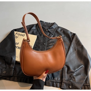 Detail of caramel brown crescent bag on leather jacket with gold zipper and adjustable strap