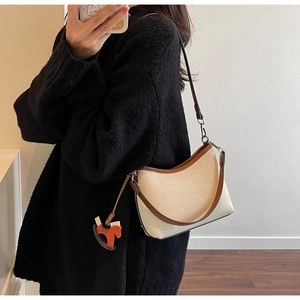 Detail of canvas underarm bag with leather trim and rocking horse charm on model