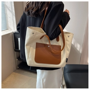 Detail of canvas tote bag showing side woven label and brown leather strap combination