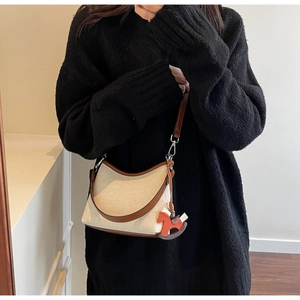 Detail of canvas underarm bag with leather trim and orange rocking horse charm accessory