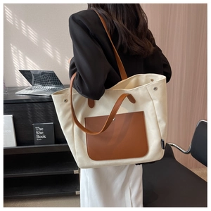 Detail of canvas tote bag featuring a brown leather pocket and metal snap button close-up