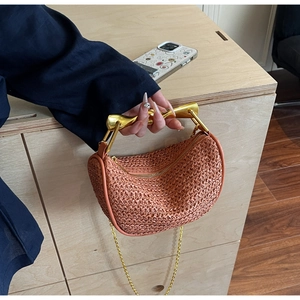 Detail of orange woven half-moon bag with golden metallic handle and chain strap
