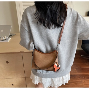 Detail of canvas underarm bag with leather trim and decorative horse charm accessory