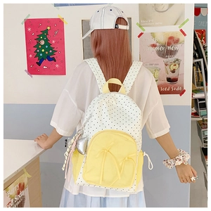 Detailed back view of a white polka dot backpack with yellow pockets on a model