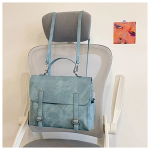 Dettaglio dello zaino vintage azzurro in pelle con doppie cinghie a fibbia su una sedia