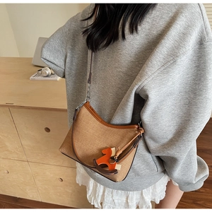 Detail of woven crescent underarm bag in beige and brown with horse charm on a model