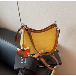 Detail of yellow woven underarm bag with brown leather trim and horse charm