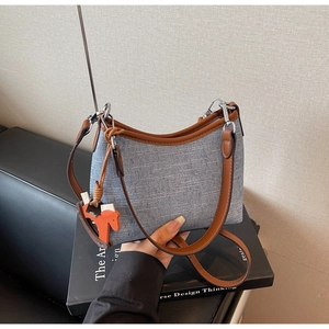 Close-up of blue denim textured crossbody bag with brown leather trim and horse charm