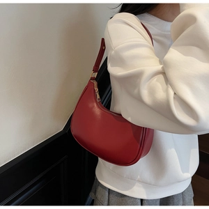Side view of red leather crescent hobo bag with gold zipper detail on white sweatshirt