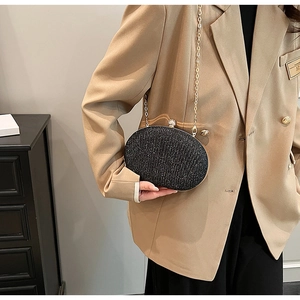 Detail of black sequined oval clutch bag with gold hardware worn as a shoulder bag