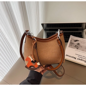 Close-up of a khaki woven shoulder bag with brown leather straps and a horse charm