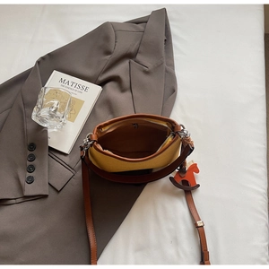 Detail of yellow fabric underarm bag with brown leather trim and horse charm