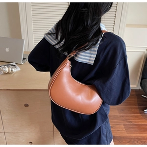 Detail of a brown crescent-shaped faux leather shoulder bag worn by a model in a modern office