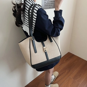 Minimalist beige woven tote bag with black leather trim and gold metal twist lock