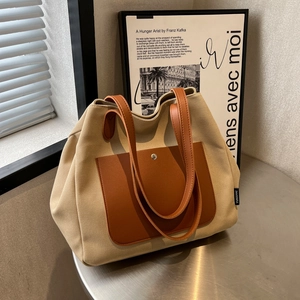 Minimalist beige canvas tote bag with brown leather pocket on a modern metal table