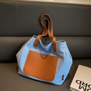 Minimalist canvas tote bag with brown leather pockets and long handles on a gray sofa