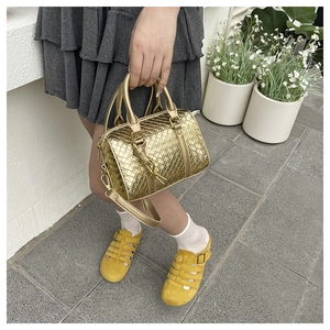 Close-up of golden metallic woven texture and handle detail on a luxury crossbody bag