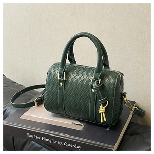 Detailed view of dark green woven Boston bag with gold hardware on a book