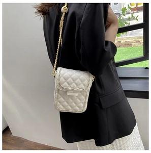 Détail du mini sac matelassé beige avec chaîne dorée et boule décorative sur veste noire