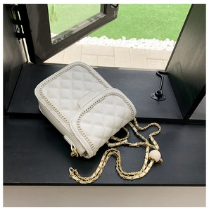 Détail d'un sac blanc matelassé avec bandoulière chaîne dorée et breloque boule