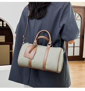 Detail of grey-green boston bag in pebble leather with brown handles shown on a model