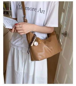Detail of a brown leather hobo bag with baseball charm and adjustable shoulder strap