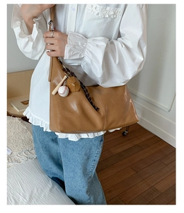 Detail of caramel brown tote bag with baseball pendant and soft leather texture