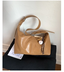 Detail of tan hobo shoulder bag featuring a unique baseball glove and bat charm