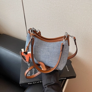 Blue denim and brown leather underarm bag with orange horse charm on a black sofa