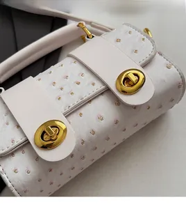 Detail of white ostrich embossed leather and polished gold metal twist lock on a shoulder bag