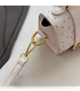 Detailed macro view of ostrich texture flap and polished gold metal buckle on white handbag