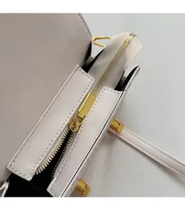 Close-up of smooth gold metal zipper on a white leather shoulder bag with black lining