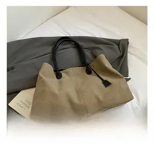 Detail show of minimalist khaki tote bag with black leather handles on white bedding