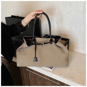 Detail of khaki canvas tote bag featuring premium black leather trim and silver metal buckle