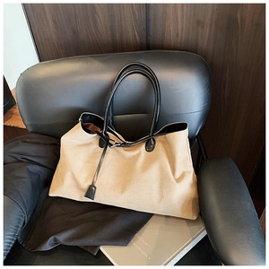 Close-up of a khaki tote bag with black leather handles on a leather chair