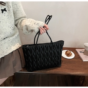 Détail d'un sac cabas noir matelassé avec texture plissée verticale et longues anses en cuir