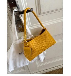 Detail of yellow woven texture shoulder bag with small circular charm hanging on door