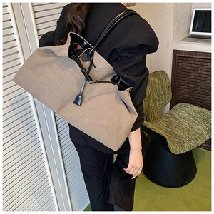 Detail of khaki canvas tote bag with black leather straps shown on a model's shoulder