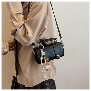 Detail of black ostrich embossed cylinder bag with gold hardware and charms on a model
