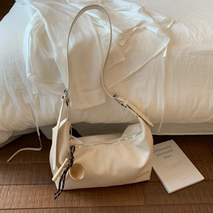 Minimalist creamy white leather tote bag with baseball charm on dark wooden floor