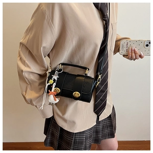 Detail of black ostrich embossed crossbody bag with gold clasps and cute goose charm