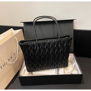 Détail du cabas noir matelassé avec plis verticaux présenté dans un coffret cadeau chic