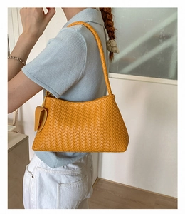 Close-up of orange woven shoulder bag with heart charm on a blue polo shirt outfit